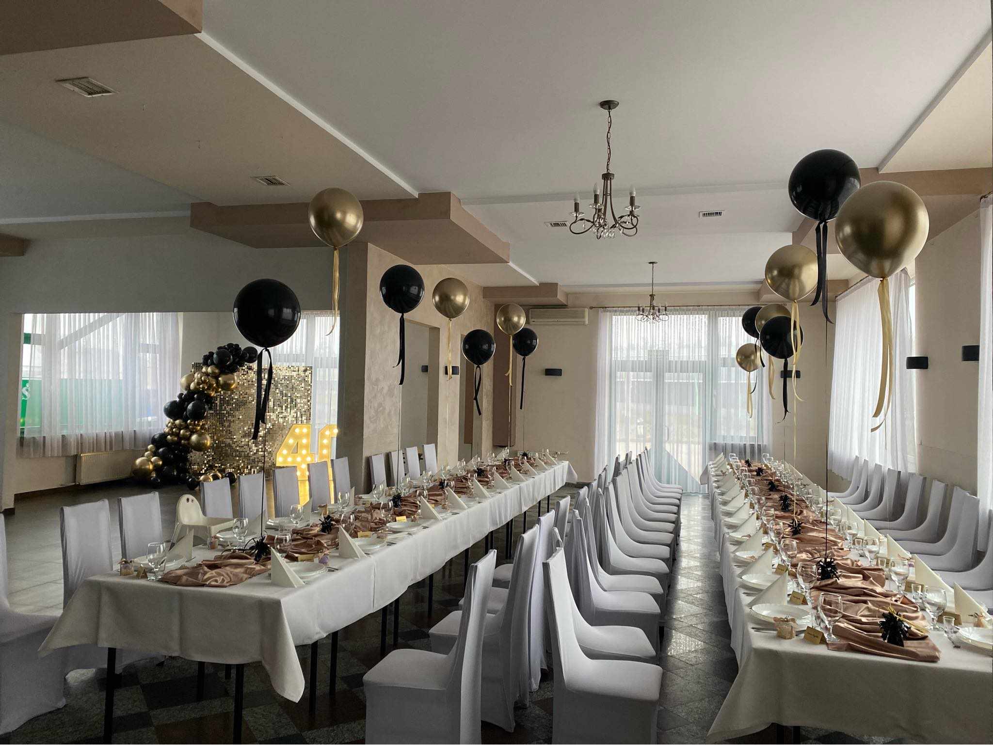Sala przyjęć w motelu ES nakryta do jubileuszu, białe pokrowce i złote balony
